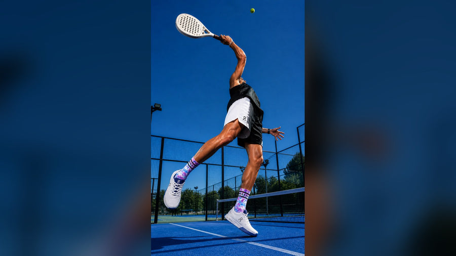 Giocatore di padel in salto per uno smash su un campo blu, con i calzini HEXXEE tie-dye ben visibili
